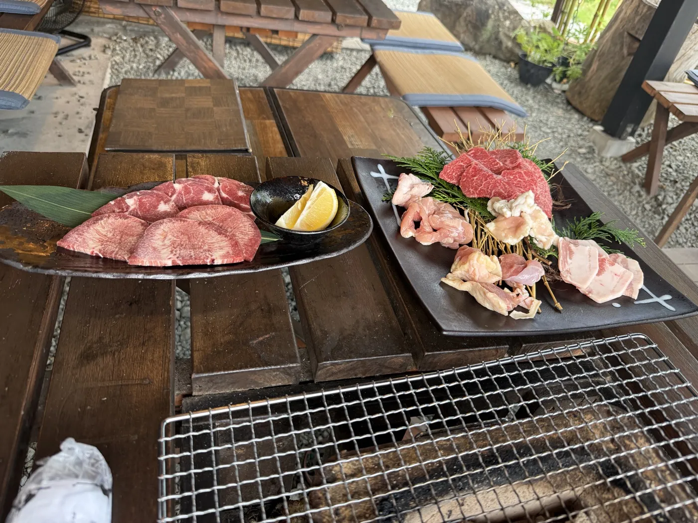 An akaushi beef platter with kalbi, horumon, chicken and pork belly beside a plate of sliced beef on a wooden charcoal table at Hyakushoya, Oguni, in September