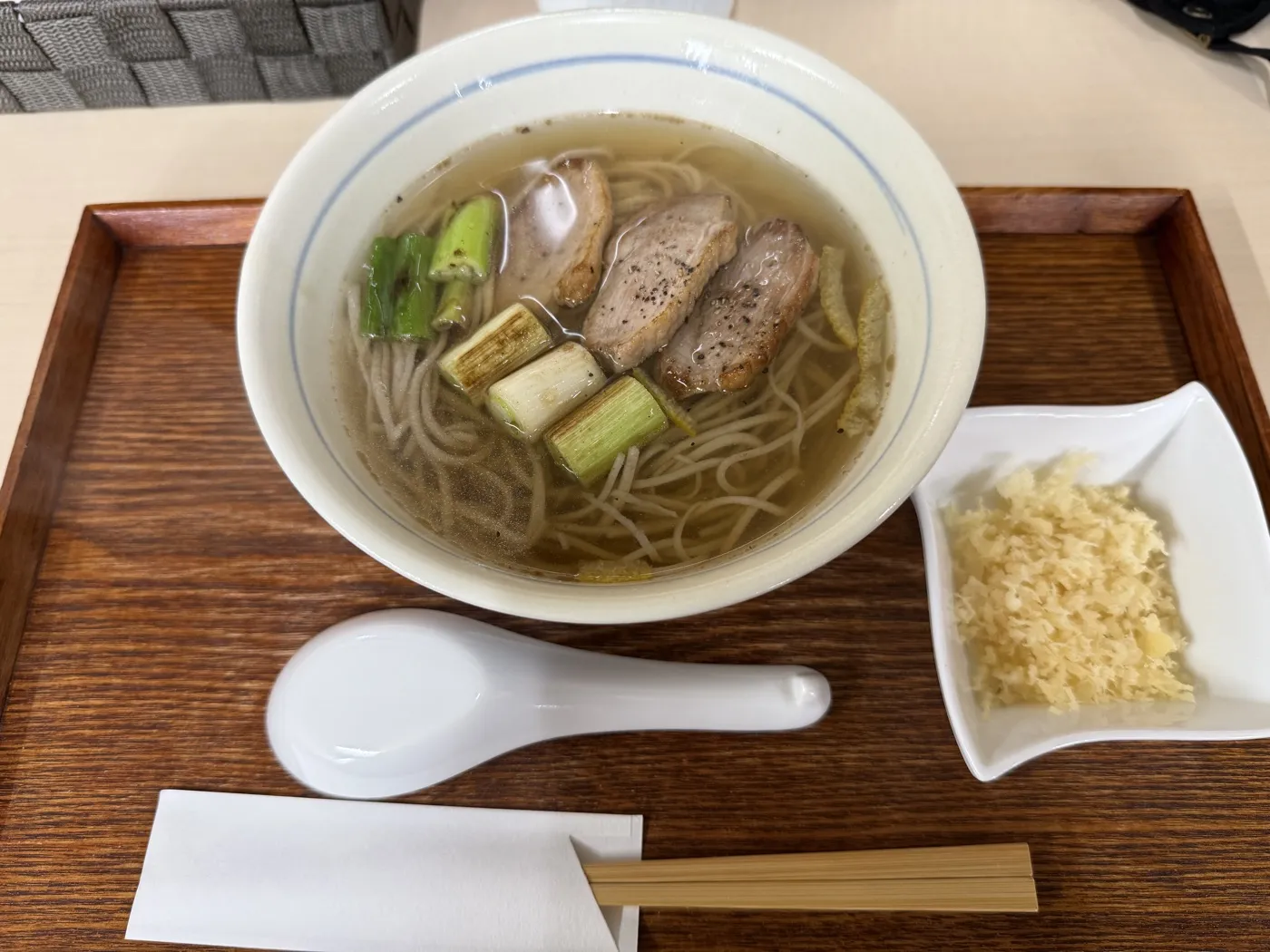 A bowl of kamo nanban soba with seared duck and grilled leeks in clear broth, a small dish of tempura crumbs beside it, on a wooden tray at Kiyoka, Minamioguni, in September