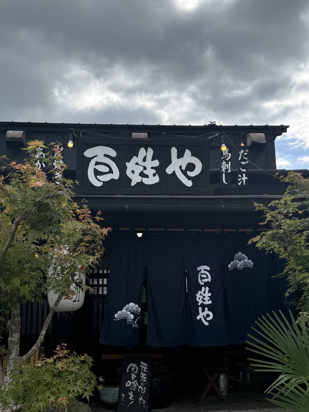 紺ののれんに「百姓や」の白い文字。軒先には「あか牛」「馬刺し」「だご汁」の看板